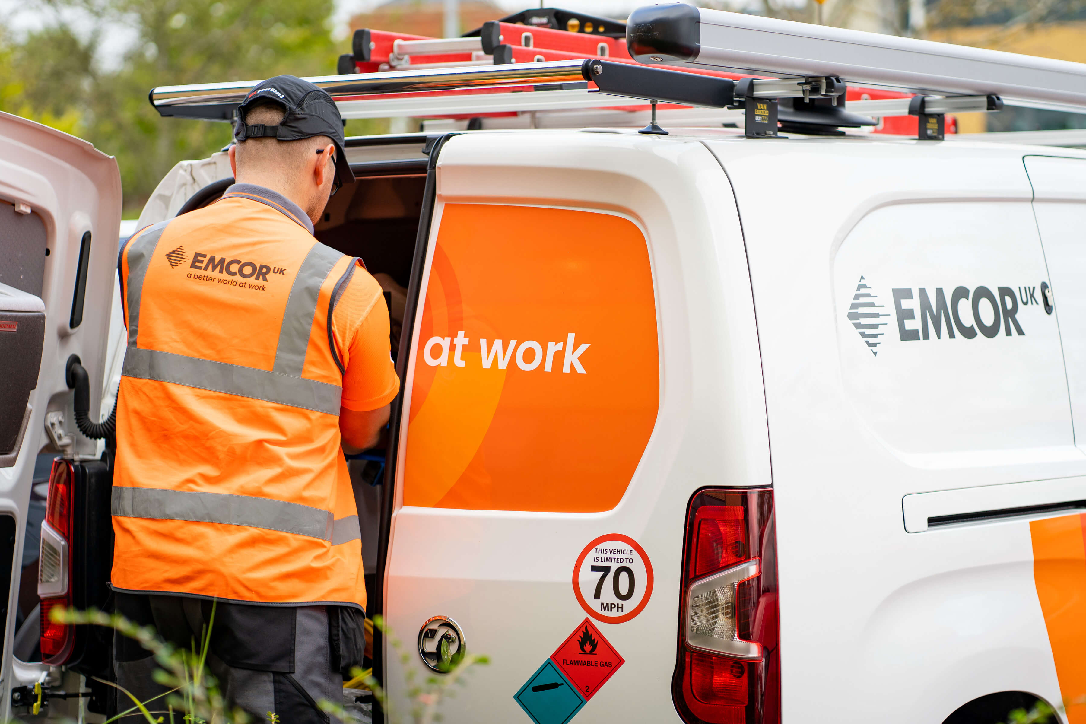 Male engineer in orange high vis jacket loading something into a branded EMCOR UK van.