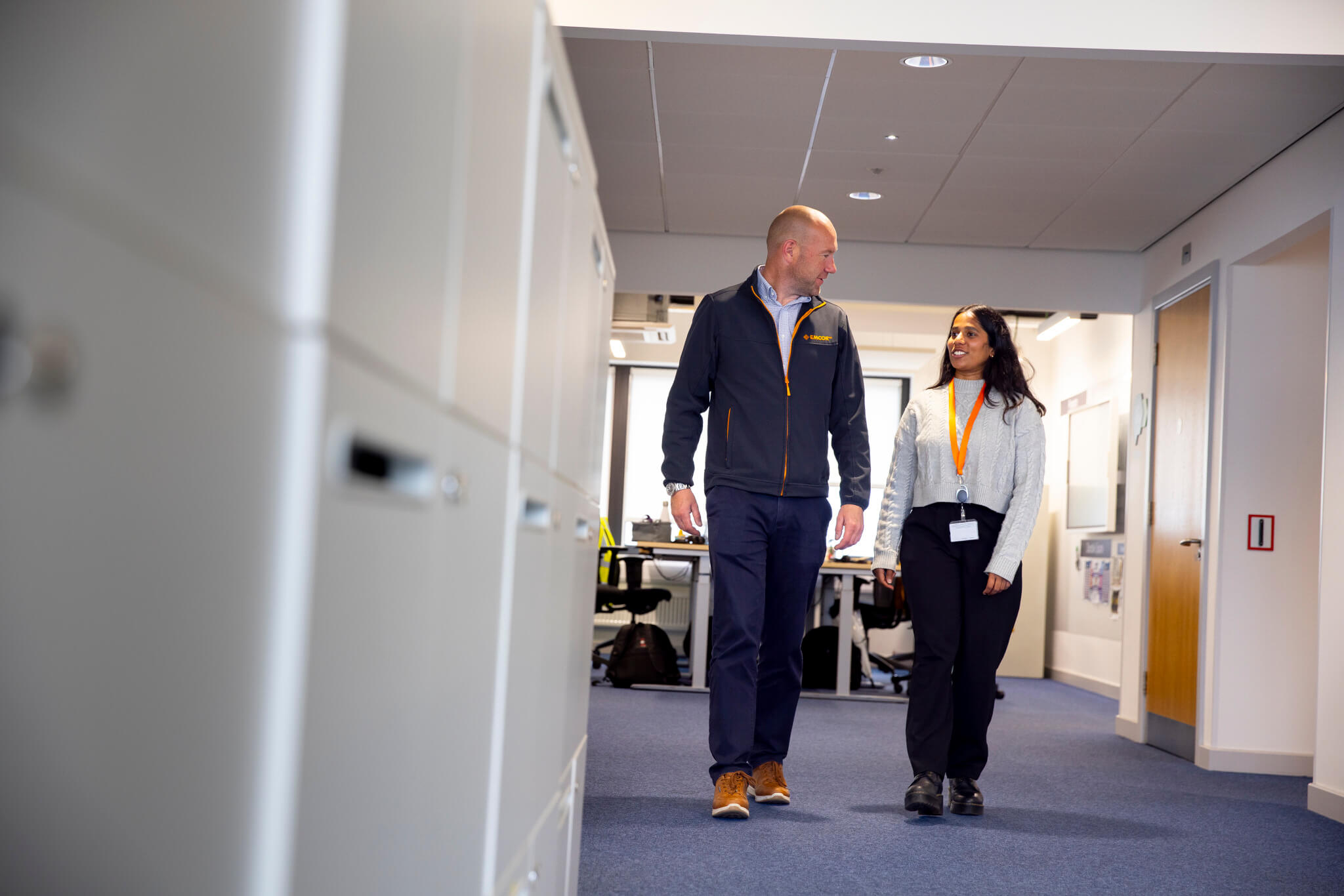 Male and female colleagues walking down an office corridor talking. 