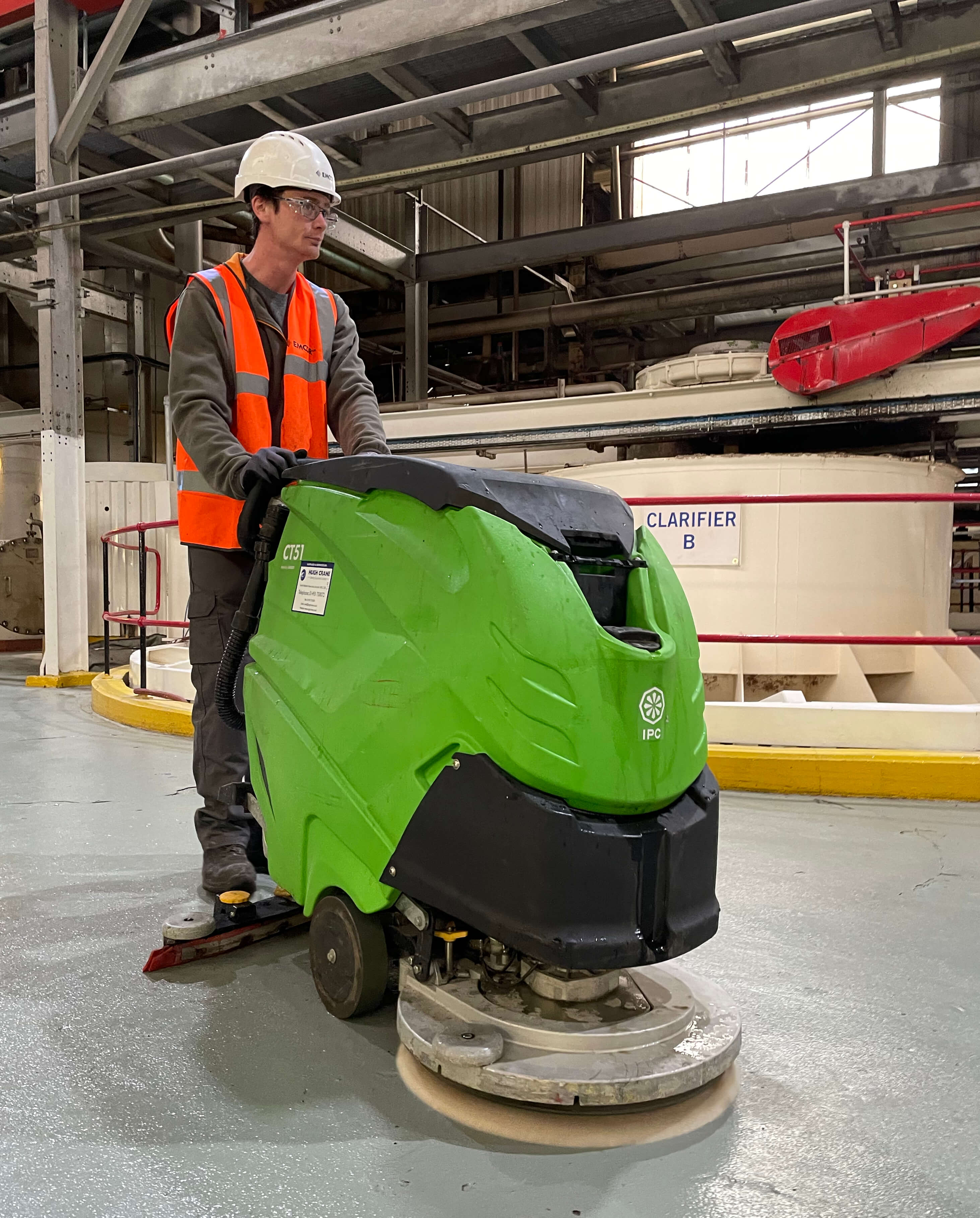 Male cleaner using a green automated industrial cleaner in a warehouse environment.