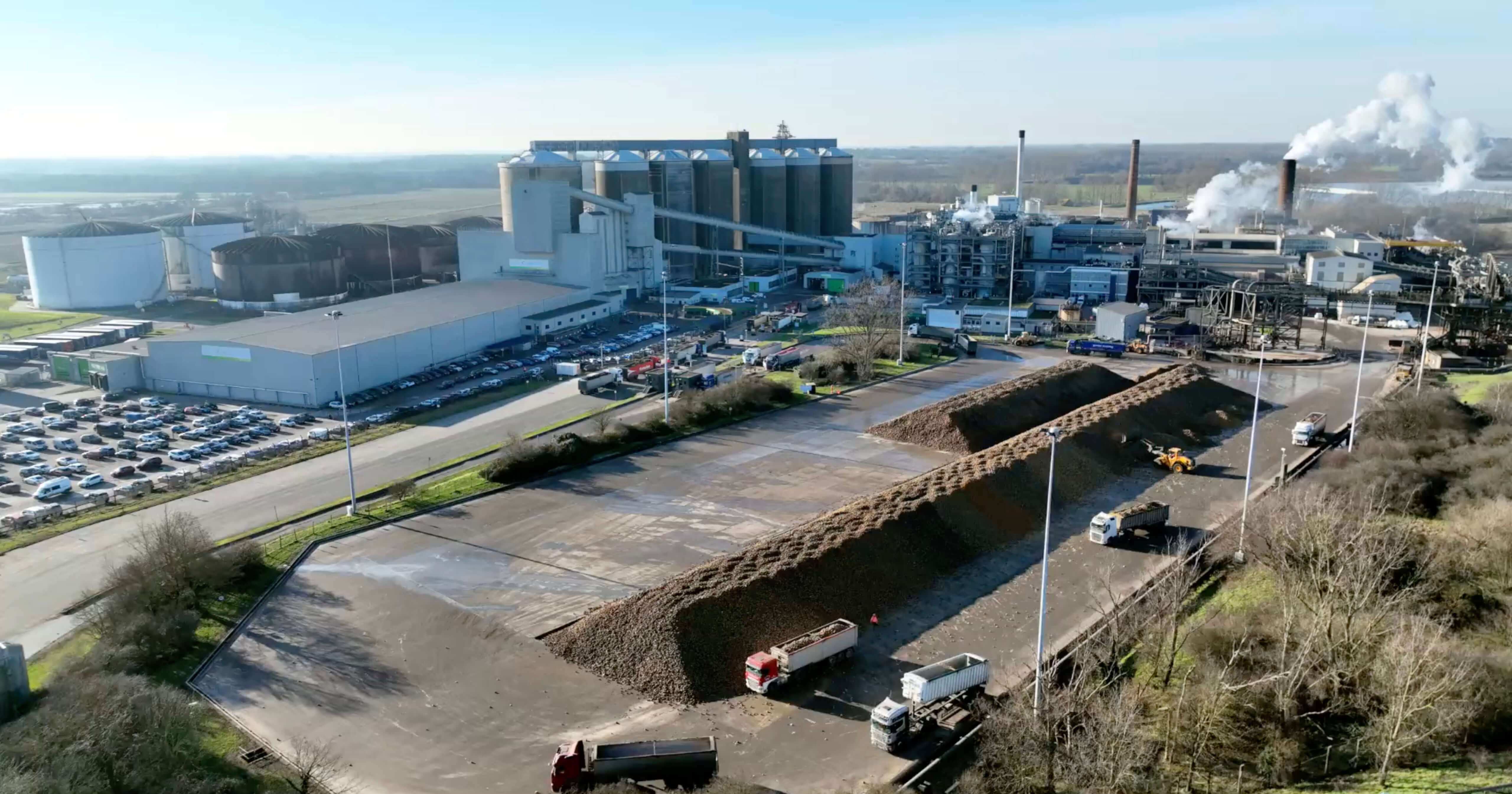 Aerial shot of industrial building on a clear day. Car park and lorries delivering goods alongside the building.