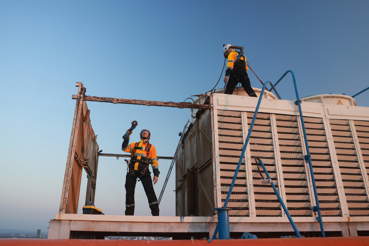 Two engineers wearing orange high vis and hard hats working on maintenance of an external cooling tower. 