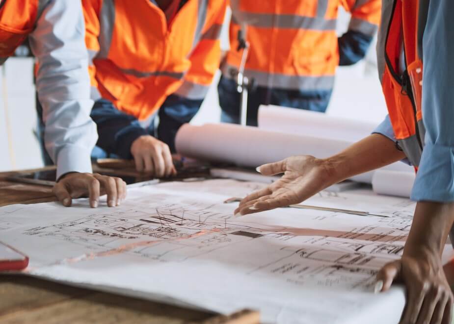 Four colleagues in hi-vis jackets looking at floor plans on a desk. 