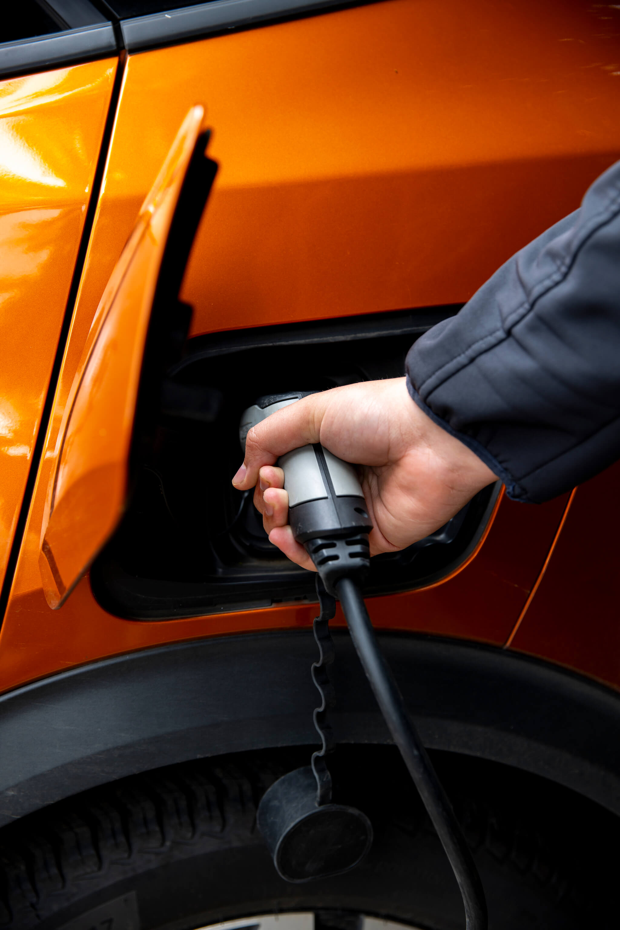 Close up of person plugging in an orange electric car.