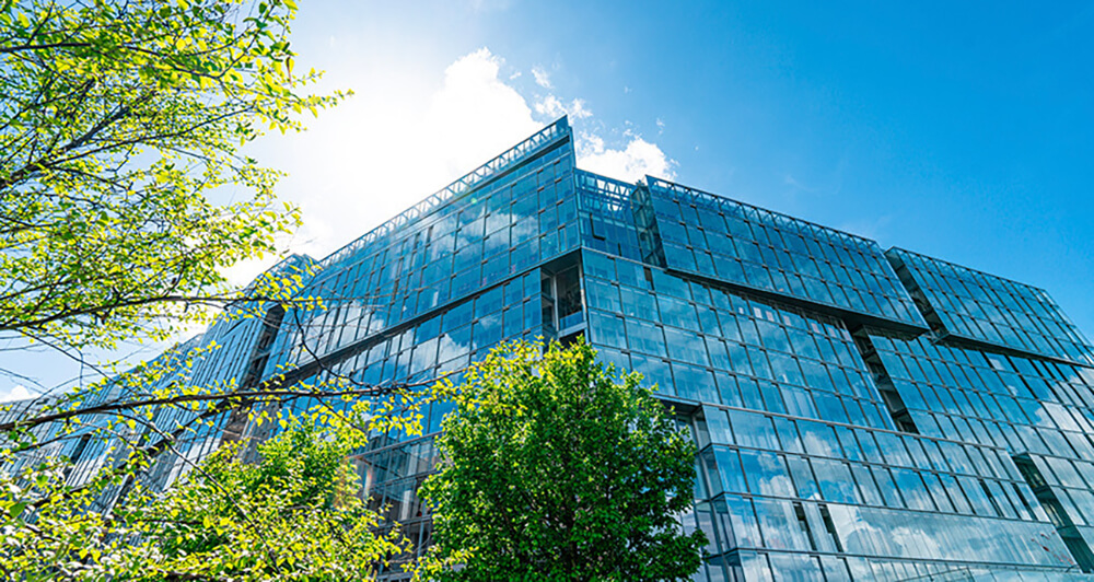 Exterior view of an all glass building with green trees next to the building