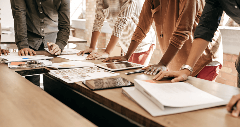 Five colleagues standing around a conference table discussing a project.