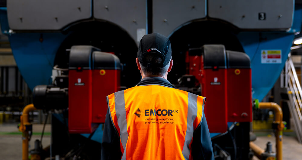 Man wearing an orange EMCOR UK vest assessing equipment