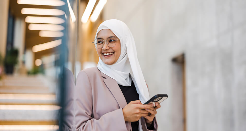 Lady with a white scarf around her head holding a phone in a corporate setting.