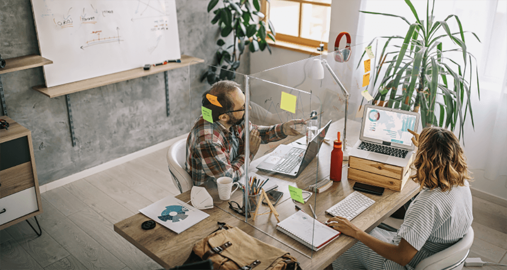 Male employee working on a laptop at a desk with glass walls and post-it notes on the walls 