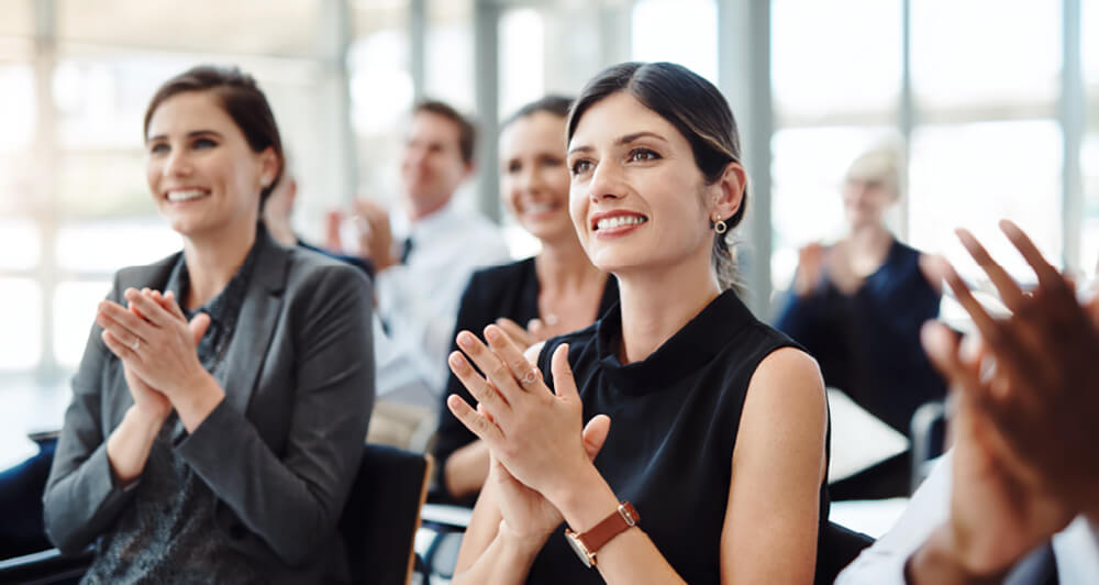 Several colleagues sitting in a conference room setting clapping.