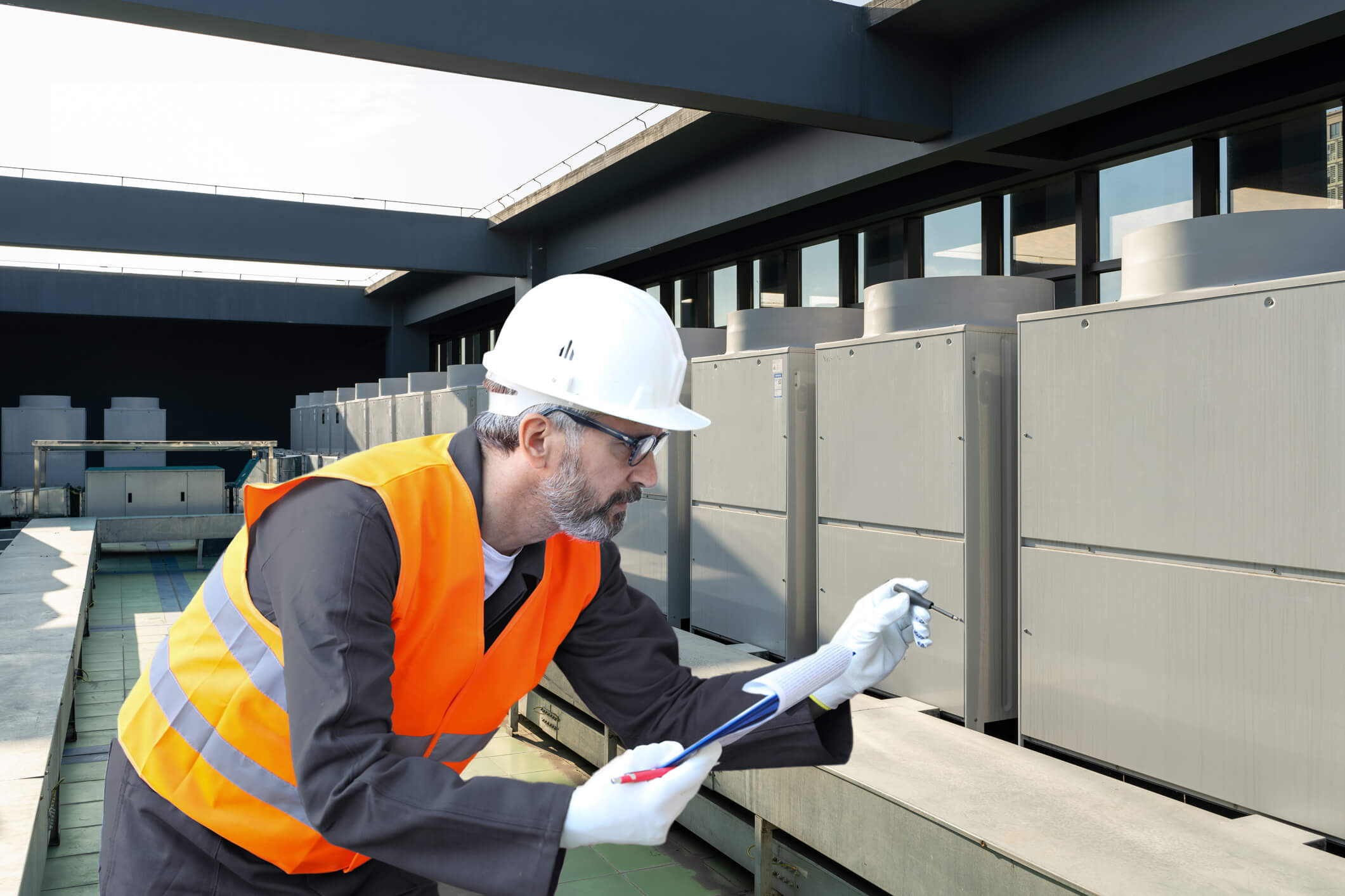 Man wearing protective clothing holding clipboard and inspecting external area of building for pests. 