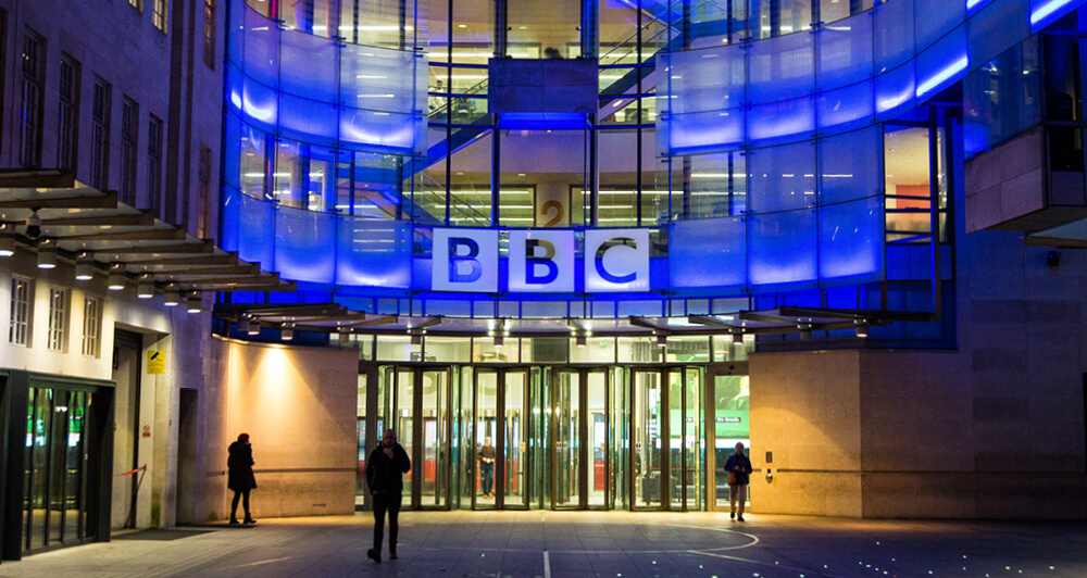 View of the BBC entrance with blue lights and people walking towards the building.