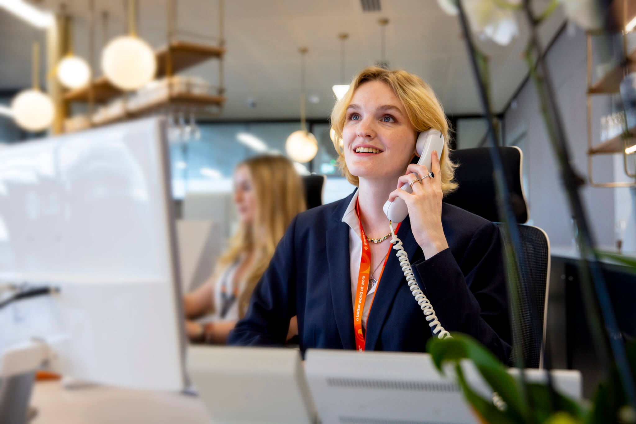 Female receptionist on the phone. Second female receptionist in the background using the computer.