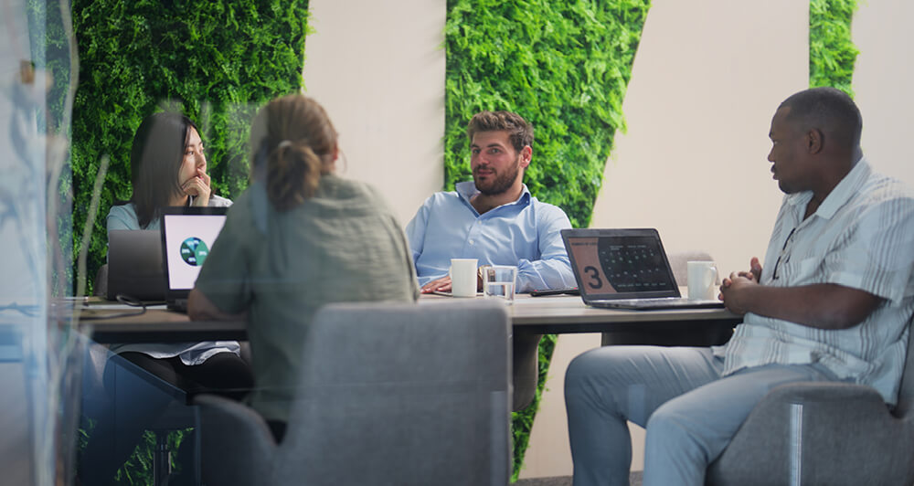 Several colleagues sitting at a conference table with a wall of plants behind them.