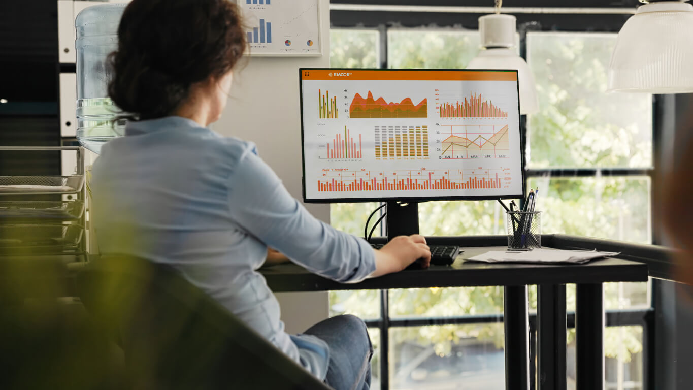 Female sat at her desk looking at integrated system controls performance data and reports on screen.