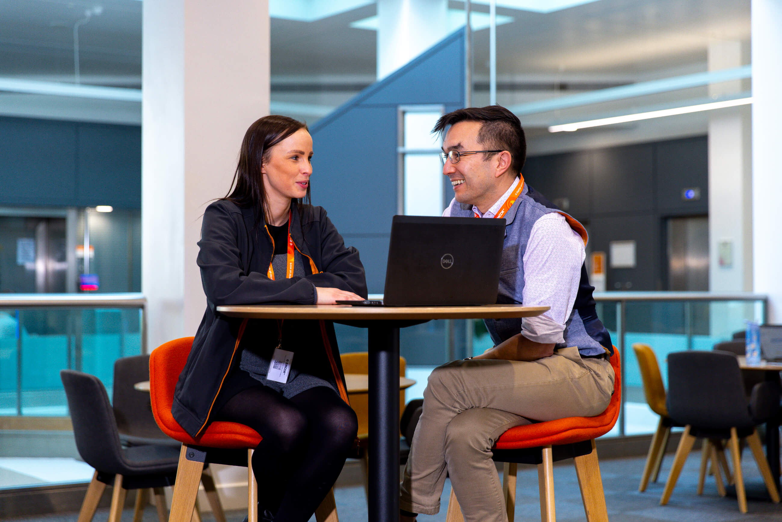 Woman and man sat at a table talking with a laptop.