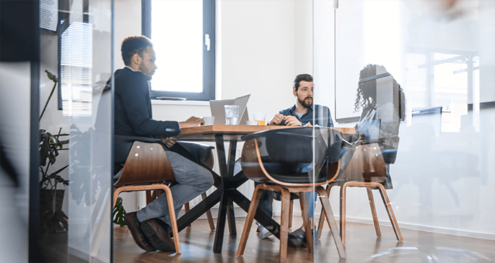 Three coworkers having a discussion in a conference room with glass walls